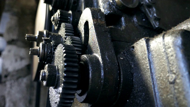关闭转动齿轮系统。低角度查看脏旋转齿轮的金属工作台在车库工作。模糊的背景。慢动作
