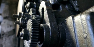 关闭转动齿轮系统。低角度查看脏旋转齿轮的金属工作台在车库工作。模糊的背景。慢动作