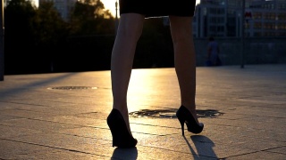 跟随女性的腿高跟鞋走在城市街道在日落时间。年轻的女商人穿着高跟鞋进城。女孩走的户外。慢动作特写侧视图视频素材模板下载
