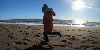 冬天阳光明媚的一天，小男孩在海滩上跑步。