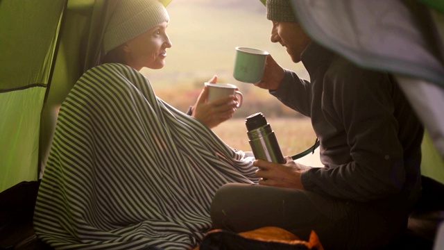 在露营帐篷里，相爱的情侣用杯子和热咖啡(茶)度过清晨