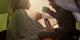 在露营帐篷里，相爱的情侣用杯子和热咖啡(茶)度过清晨