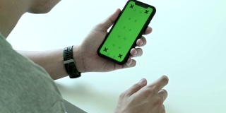 男人使用，滚动和看智能手机的绿色屏幕和色度键在家里