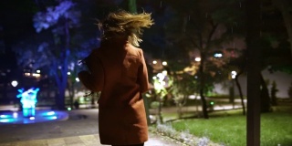 美丽的女人在雨中在公园里奔跑。街上的红头发女人。慢动作
