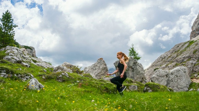 女运动员在一个被山包围的草地上的草地和岩石小径上跑步