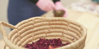 一个篮子的特写侧视图，满是干花。镜头移动，展示了女孩如何用杵将干燥的玫瑰花瓣磨成粉末。