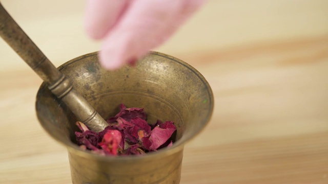 特写镜头，一个女孩正在用杵将干燥的玫瑰花瓣磨成粉末。