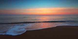 海面和海滩上的日出。海浪冲刷着沙滩
