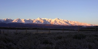 令人难以置信的景色。清晨的山上，霜在草地的前景。黄色的阳光在雪峰的背景