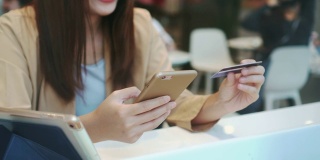 一名亚洲女性使用信用卡和手机进行网上购物的4k视频场景，在百货公司的联合办公空间，技术货币钱包和在线支付概念，信用卡模型