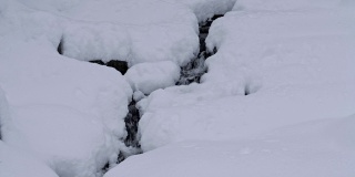 冬天，深雪，一条小溪，白雪覆盖的石头，白色的帽子，特写镜头，实时