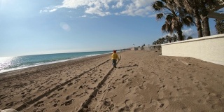 冬天阳光明媚的一天，小男孩在海滩上跑步。