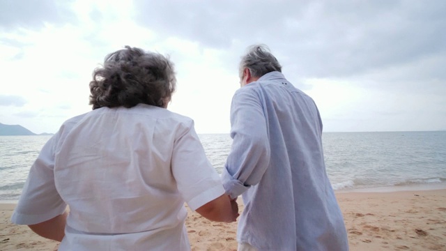 老人和妻子带着幸福的情绪一起跑向海滩。有生活方式、情感和退休观念的人。慢动作镜头。