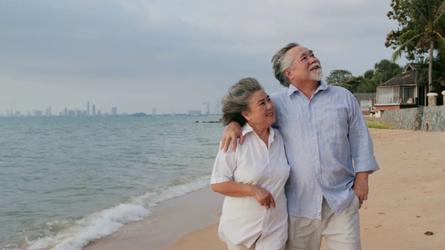 年老的亚洲夫妇走在海滩上一起笑。有生活方式、情感和退休观念的人。