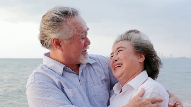 年长的亚洲夫妇站在海滩上，心情愉快。有生活方式、情感和退休观念的人。