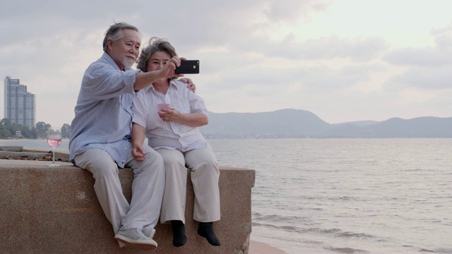 资深亚洲夫妇使用智能手机自拍在海滩上与幸福的情感在一起。有生活方式、退休和科技观念的人。