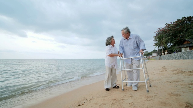 老人在沙滩上与walker和他的妻子一起锻炼。人有医疗、医疗和退休的概念。