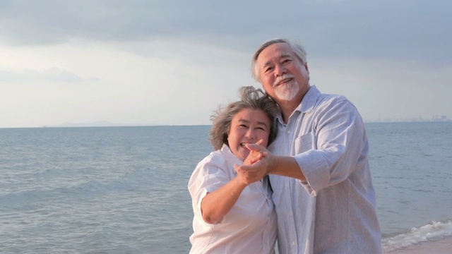 亚洲高年级情侣在沙滩上跳舞一起笑。有生活方式、情感和退休观念的人。