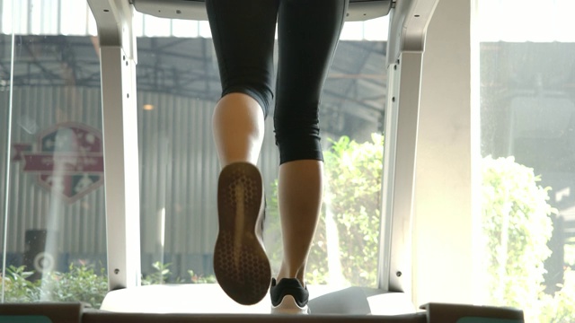 亚洲女性在健身房里跑步机上跑步的背影。慢动作。