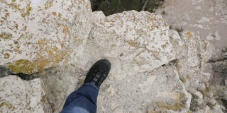 从荒芜边缘的最高点看向岩石的边缘和靴子向下移动进入深渊