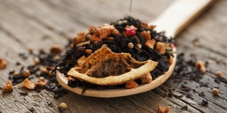 黑果茶的干叶与肉桂，苹果，橘子，香菜，小豆蔻，丁香和红辣椒倒在木勺的木质背景