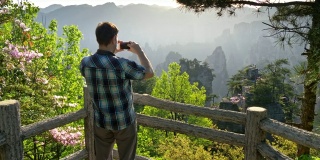 在一个阳光明媚的日子里，一名游客在武陵源用他的智能手机拍摄悬崖峭壁的风景。张家界,中国。UHD