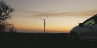 日落时风力发电站背景上的汽车