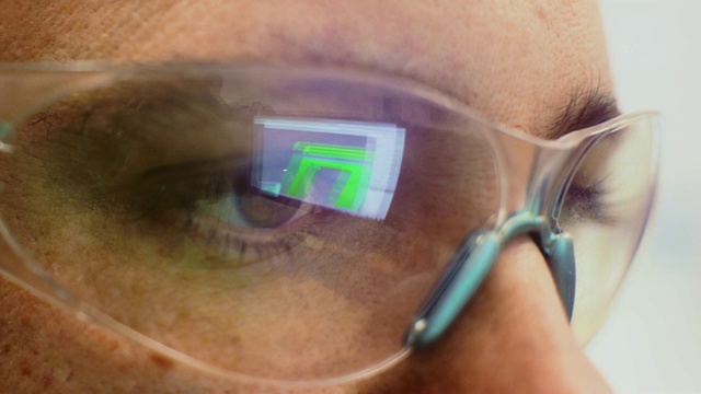 一个高加索技术员的眼睛的特写镜头与反射的电脑屏幕在他的保护眼镜在一个室内办公室