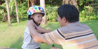 爸爸把头盔戴在亚洲2 - 3岁蹒跚学步的小男孩身上，爸爸和儿子玩平衡自行车