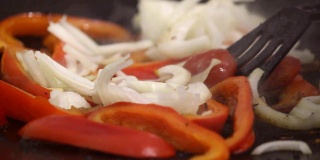 一碟蔬菜片。辣椒和洋葱在煎锅里炸，用热油或油，在明火上煮。
