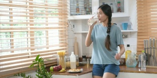年轻美丽的亚洲女人吃面包，喝牛奶，在厨房跳舞，快乐健康的生活方式
