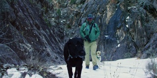 一名四十多岁的白人男子穿着登山装备，带着他的狗在冬天散步和爬上科罗拉多西部高沙漠的岩层(靠近科罗拉多国家纪念碑-大路口，科罗拉多州)