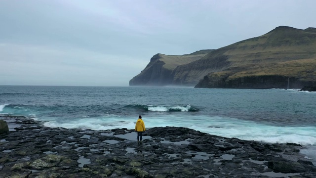 航拍的女人在黄色雨衣看风景的海边在法罗群岛