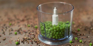 慢镜头，宏镜头:自家种的美味豌豆掉进了一个塑料食物搅拌机里。