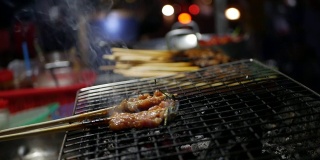 街头小吃摊贩在夜市准备和出售烤猪肉串，烧烤炸猪肉。Closeup.4k