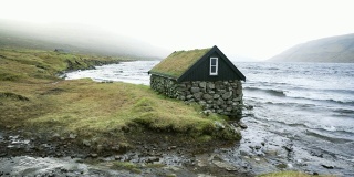 在法罗群岛的海边，屋顶覆盖着苔藓的小屋的风景