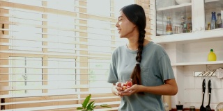 年轻的亚洲女人在家里的厨房里吃着幸福的草莓，人们健康的生活方式