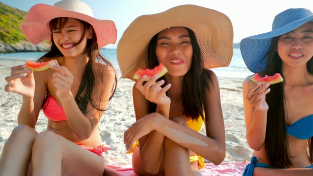 三个性感的女人笑着吃冷西瓜片，在海滩上玩，暑假。假期——iStock