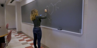 女大学生一边用智能手机一边在黑板上写字