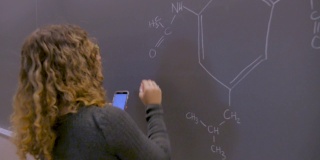 年轻的学生用智能手机在黑板上解决化学问题