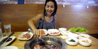 年轻美丽的亚洲女人烧烤烧烤在韩国锅。特写猪肉片在韩国餐厅烤。