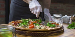 厨师厨师在披萨店的木桌上用滚筒刀切披萨。在意大利餐厅切热披萨切片。制作传统意大利食品的过程。食品的概念