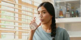 特写年轻的亚洲妇女在厨房里喝水在家，人们健康的生活方式