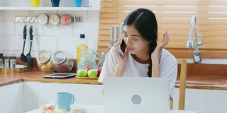 年轻美丽的亚洲女人谈论智能手机与幸福，坐在厨房吃零食在家里，人们在电话，生活方式