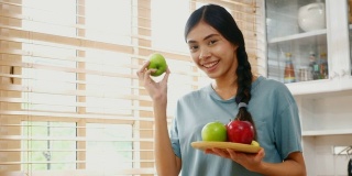 年轻的亚洲女人拿着苹果与幸福在家里的厨房，人们健康的生活方式