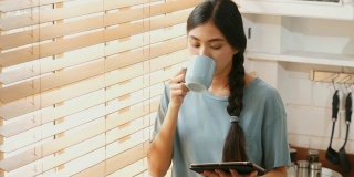 年轻美丽的亚洲女人在家里的厨房里一边喝着咖啡一边用着数字平板电脑，人和科技，Z一代的生活方式
