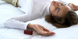 女子服用过量药物，躺在木地板上，药瓶开着。过量用药和自杀的概念。