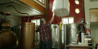 在一个室内酒精蒸馏厂，一名白人男子用龙门起重机和绞车移动一大袋甘蔗