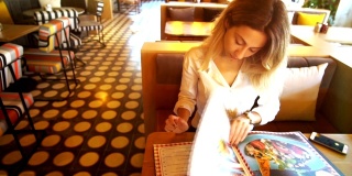 年轻漂亮的女人坐在餐馆或咖啡馆里看着菜单。
