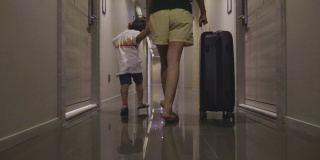 亚洲女性和小男孩客人走进酒店房间与她的手提箱。